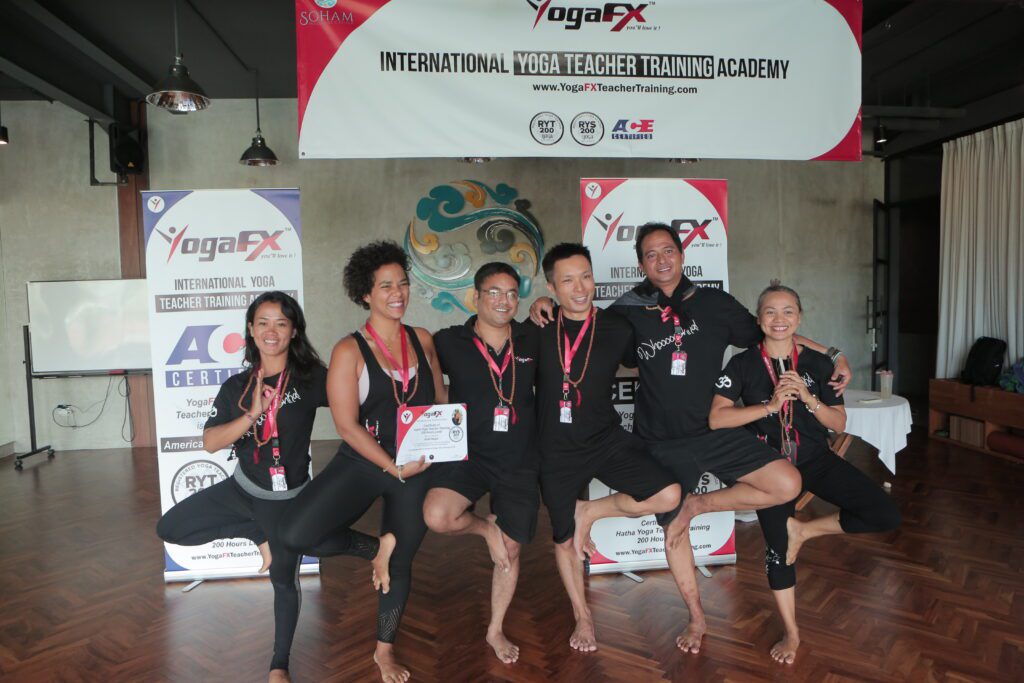 YogaFX teacher training cohort in Tree Pose with their certificates after completing the six-day Bikram 26&2 intensive in Bali