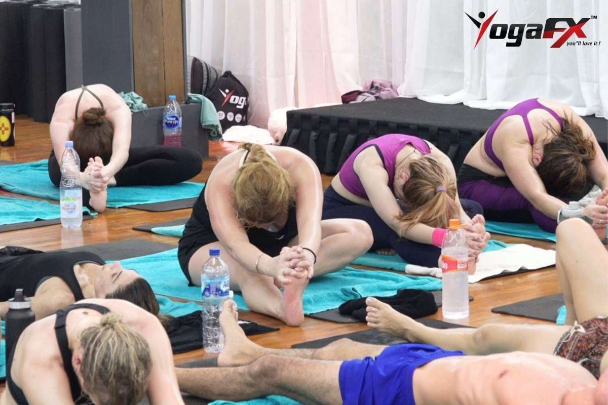 Students in a seated forward fold on teal mat towels, with water bottles and spare towels at the edge of each mat