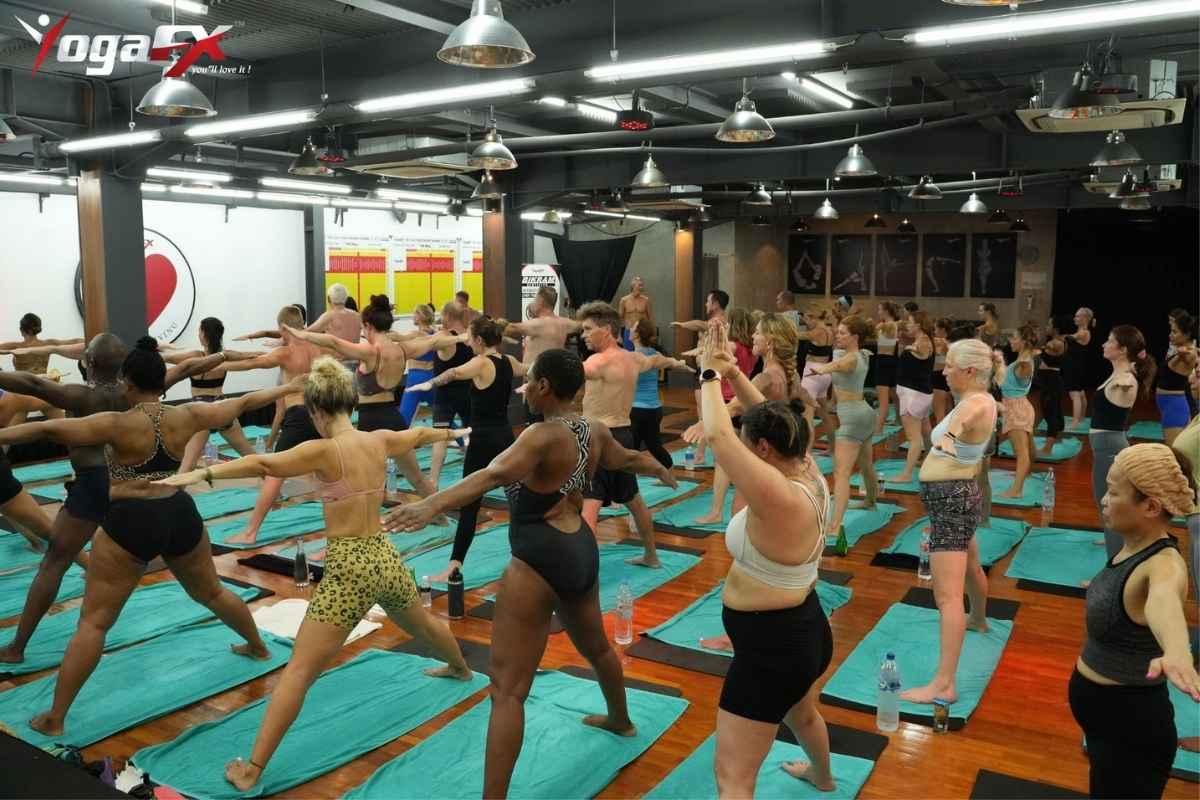 Standing series in a Bali hot yoga class with each student on a teal hot yoga mat towel laid over a mat, water bottles beside them