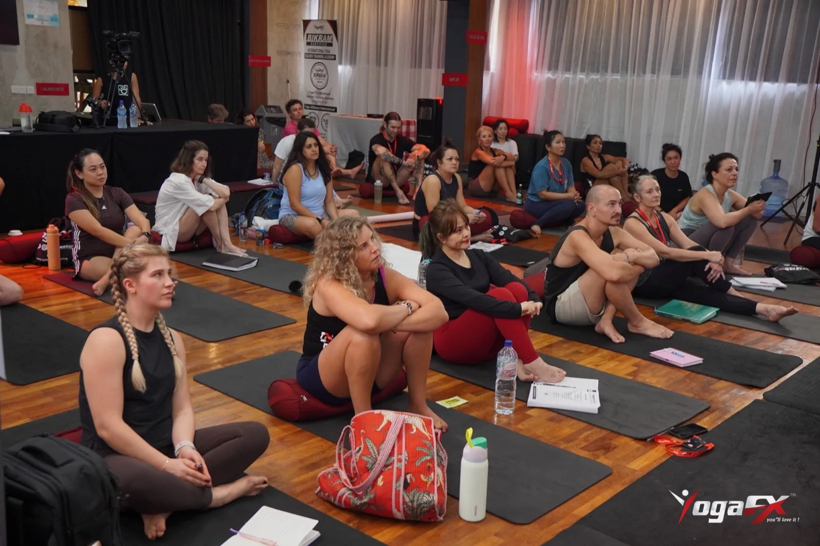 Students sitting on mats with water bottles and notebooks in the YogaFX Bali studio, resting and listening before planning a sauna after hot yoga